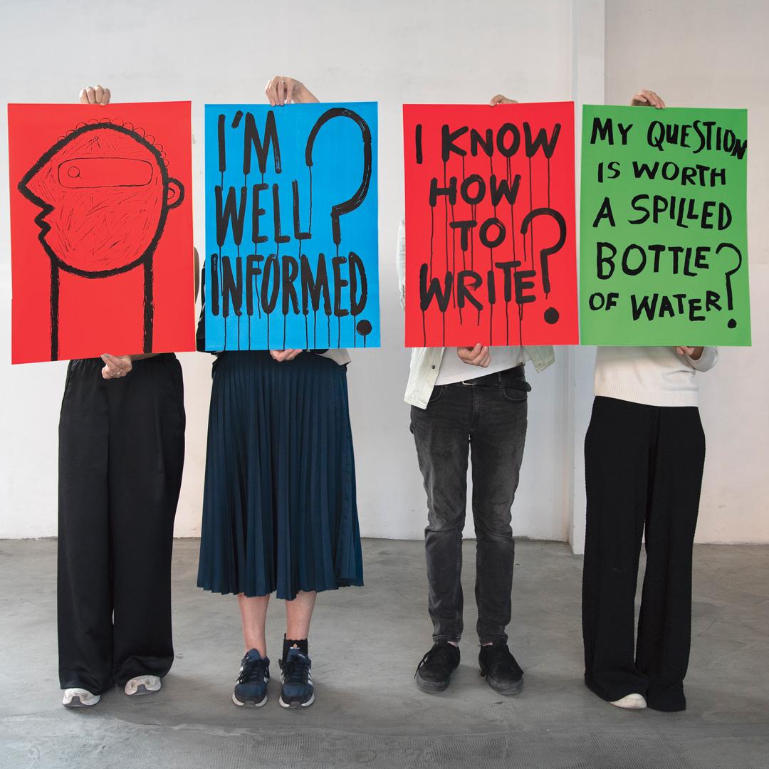 Cztery osoby trzymają przed sobą kolorowe plakaty z pytaniami