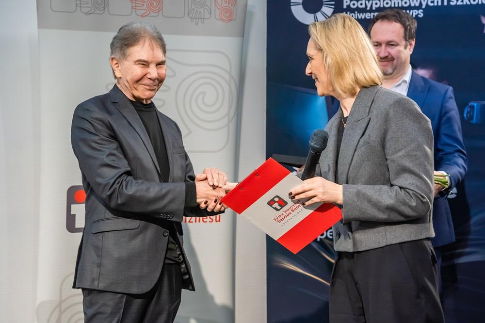 Profesor Cialdini i przedstawicielka Polskiego Towarzystwa Trenerów Biznesu ściskają sobie dłonie przy wręczaniu nagrody
