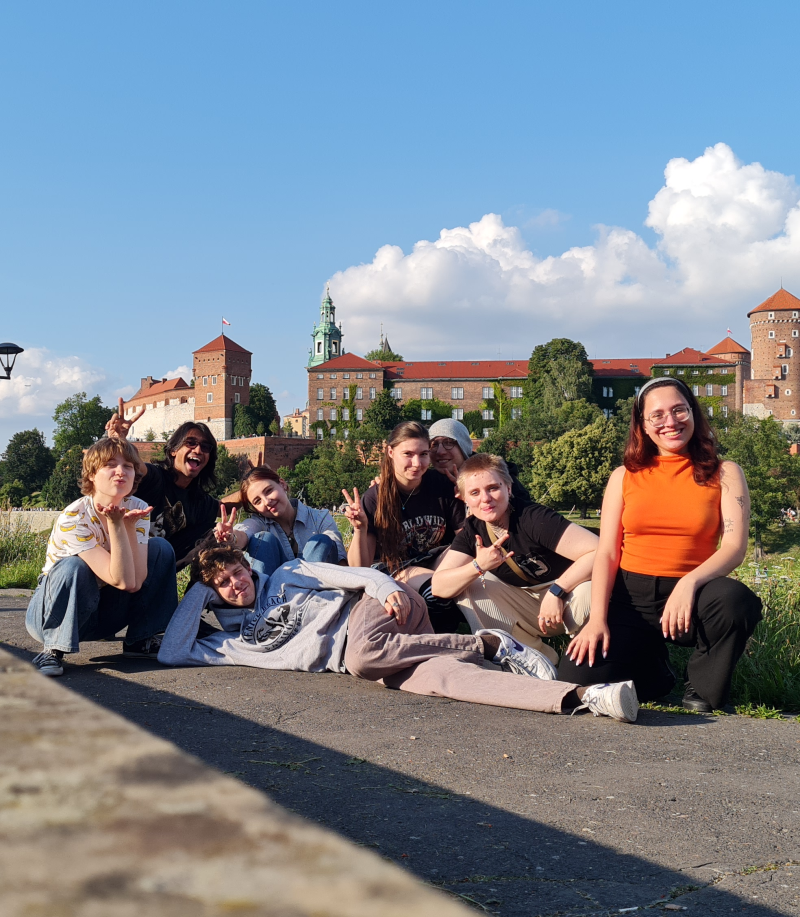 Ośmioro uśmiechniętych, rozluźnionych studentek i studentów pozuje do zdjęcia na tle Wawelu