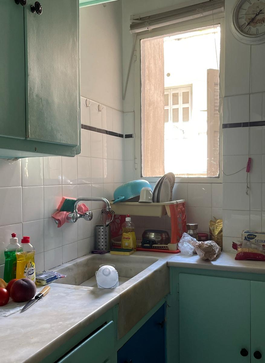 Wnętrze małej kuchni z niewielkim oknem, na blacie typowe akcesoria kuchenne i naczynia.