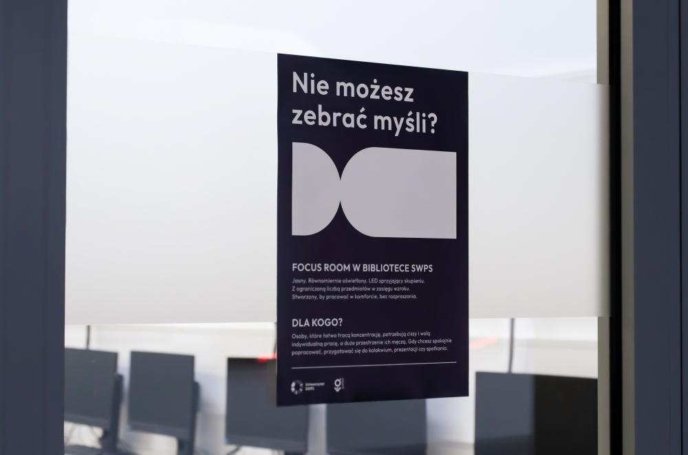 Czarny plakat na przeszklonych drzwiach z białym symbolem i dużym nagłówkiem „Nie możesz zebrać myśli? FOCUS ROOM W BIBLIOTECE SWPS”.