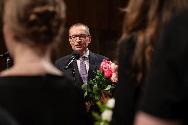 Rektor Uniwersytetu SWPS, profesor Roman Cieślak mówi do mikrofonu, trzymając bukiet kwiatów
