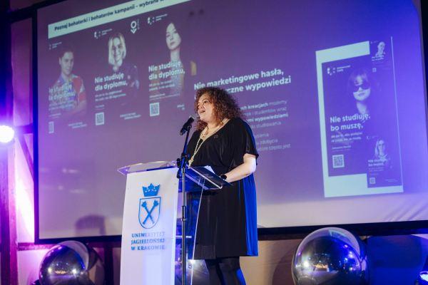 Gala Nagrody Stowarzyszenia PRom 2026. Ewelina Kolendowicz-Ossowska przemawia z mównicy z logo Uniwersytetu Jagiellońskiego. W tle slajd z informacjami o kampanii „Nie studiuję dla dyplomu”