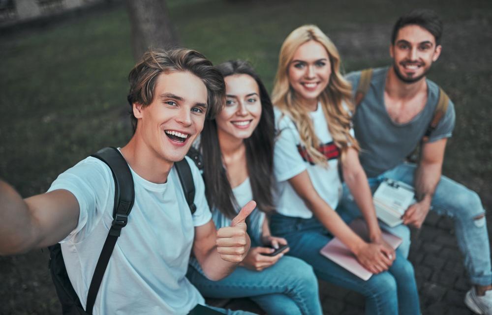 Grupa młodych uśmiechniętych ludzi, siedzących na ławce w parku