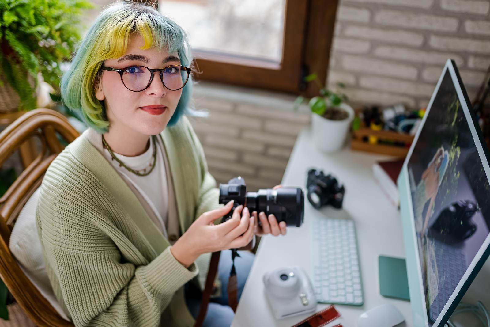 Młoda dziewczyna z aparatem fotograficznym siedząca przed komputerem.