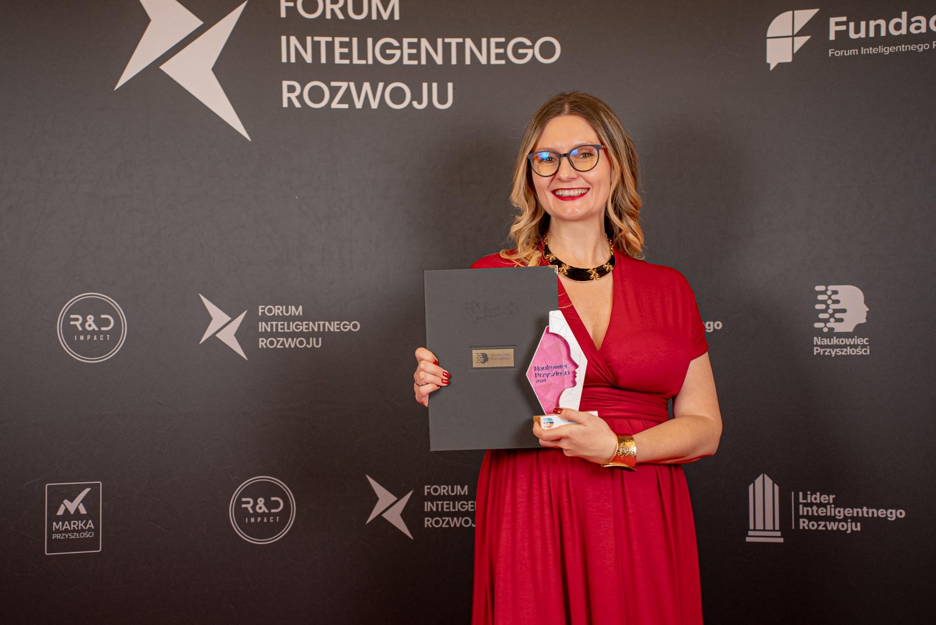 Dr Wróblewska stojąca ze statuetką na czerwonym dywanie, w tle widać ściankę z napisem Forum Inteligentnego Rozwoju