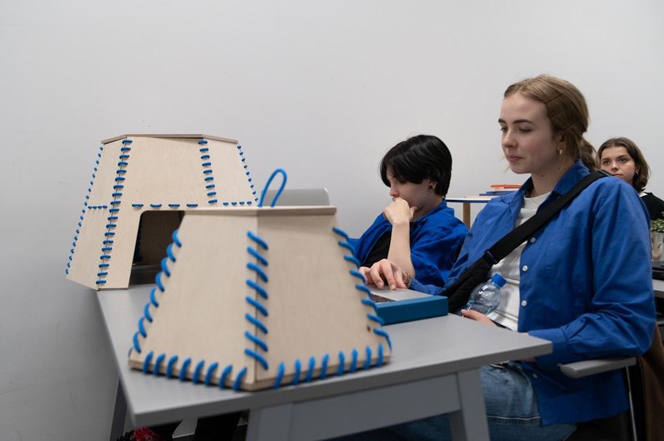 Studentki siedzące przy stoliku, na którym stoją ich projekty wycięte ze sklejki